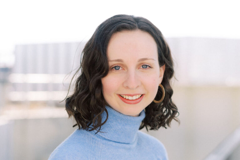 A woman, Jessica Long, leans against a railing with a light blue turtleneck.
